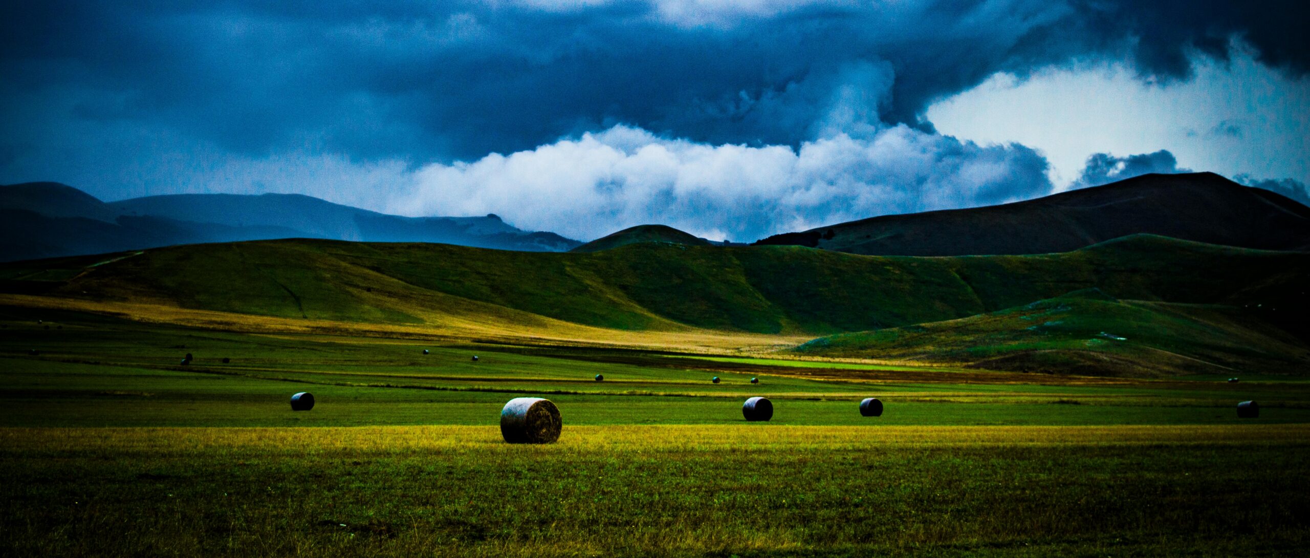 Gorgeous rolling hills and hay bales under a dramatic sky in Castelluccio, Umbria.