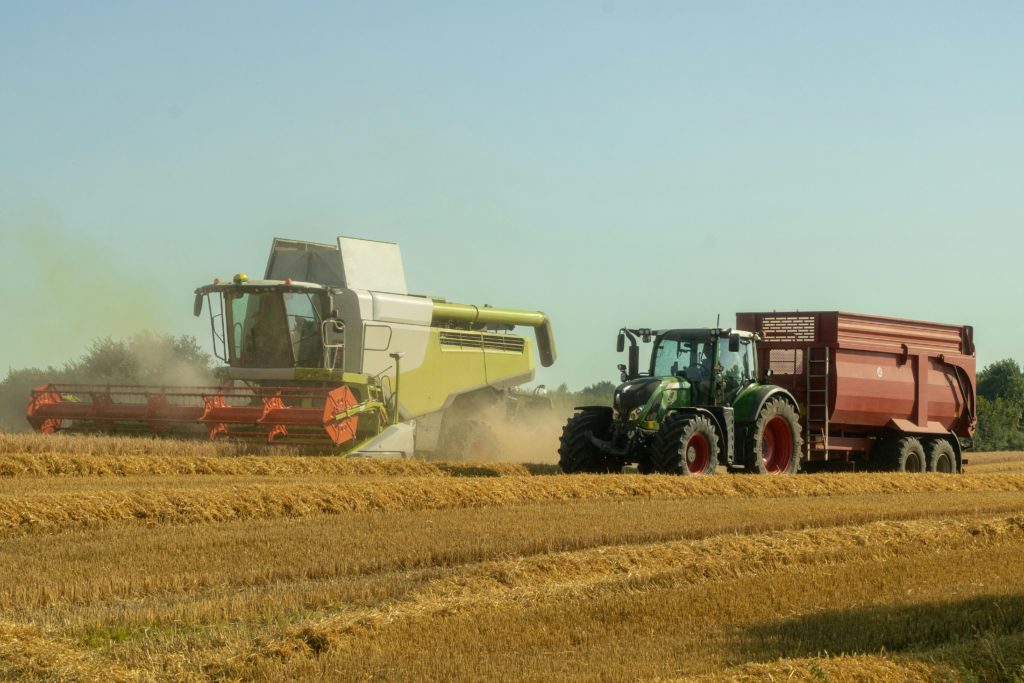 pexels-photo-12982187-12982187 A combine harvester and tractor operate in a sunlit wheat field, capturing the essence of modern agriculture.